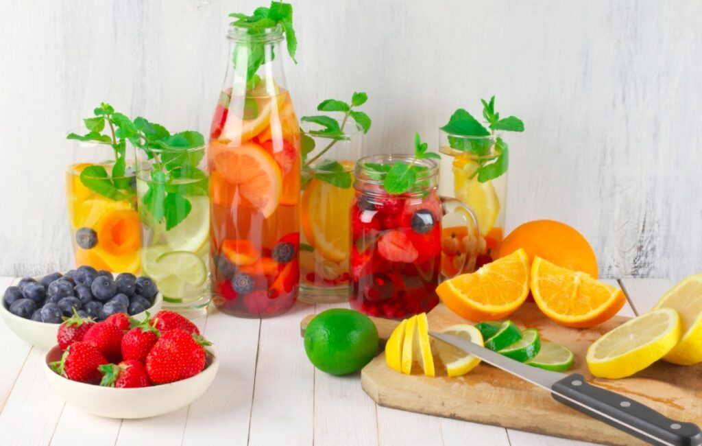 idratazione i consigli di beauty Med un tavola riccamente imbandita e colorata con frutta anche tagliata a spicchi e bicchieri e bottiglie con liquidi idratanti e rinfrescanti