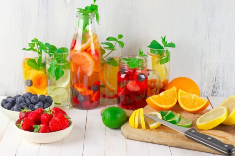 idratazione i consigli di beauty Med un tavola riccamente imbandita e colorata con frutta anche tagliata a spicchi e bicchieri e bottiglie con liquidi idratanti e rinfrescanti